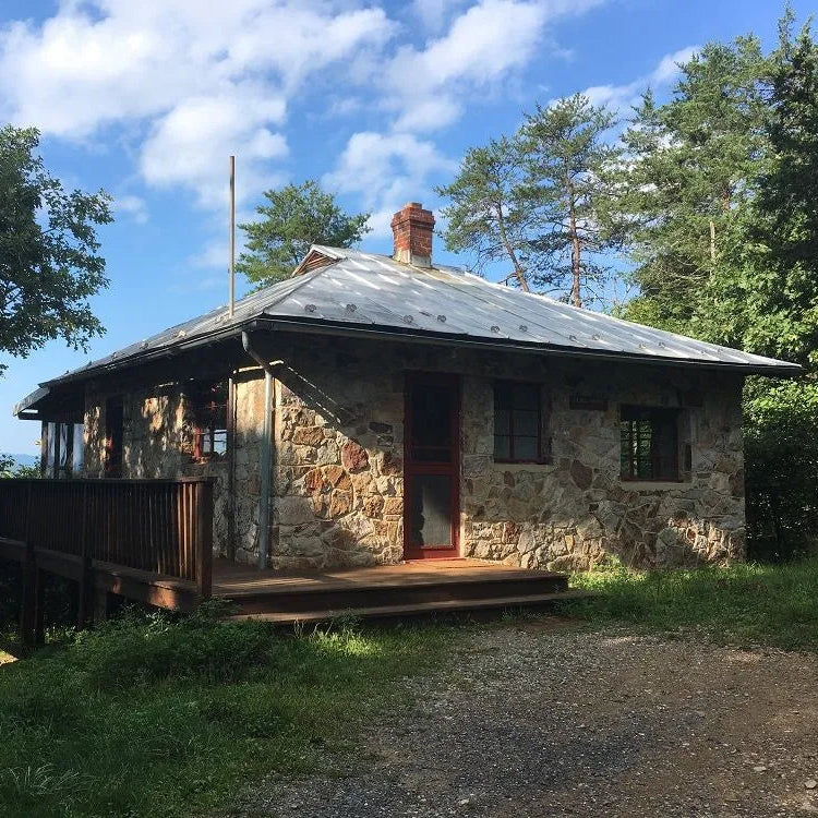 Stone cabin with a wooden deck surrounded by trees on a sunny day.